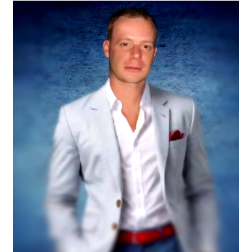 Portrait of the founder, Jay Pascall dressed in a light grey blazer over a white dress shirt. He is wearing a red belt and a pocket square, standing against a textured blue background, with a confident yet relaxed posture.